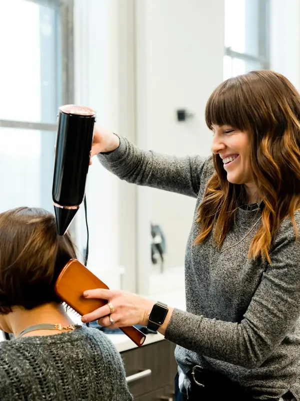 Friseurin föhnt einer Kundin die Haare im Salon